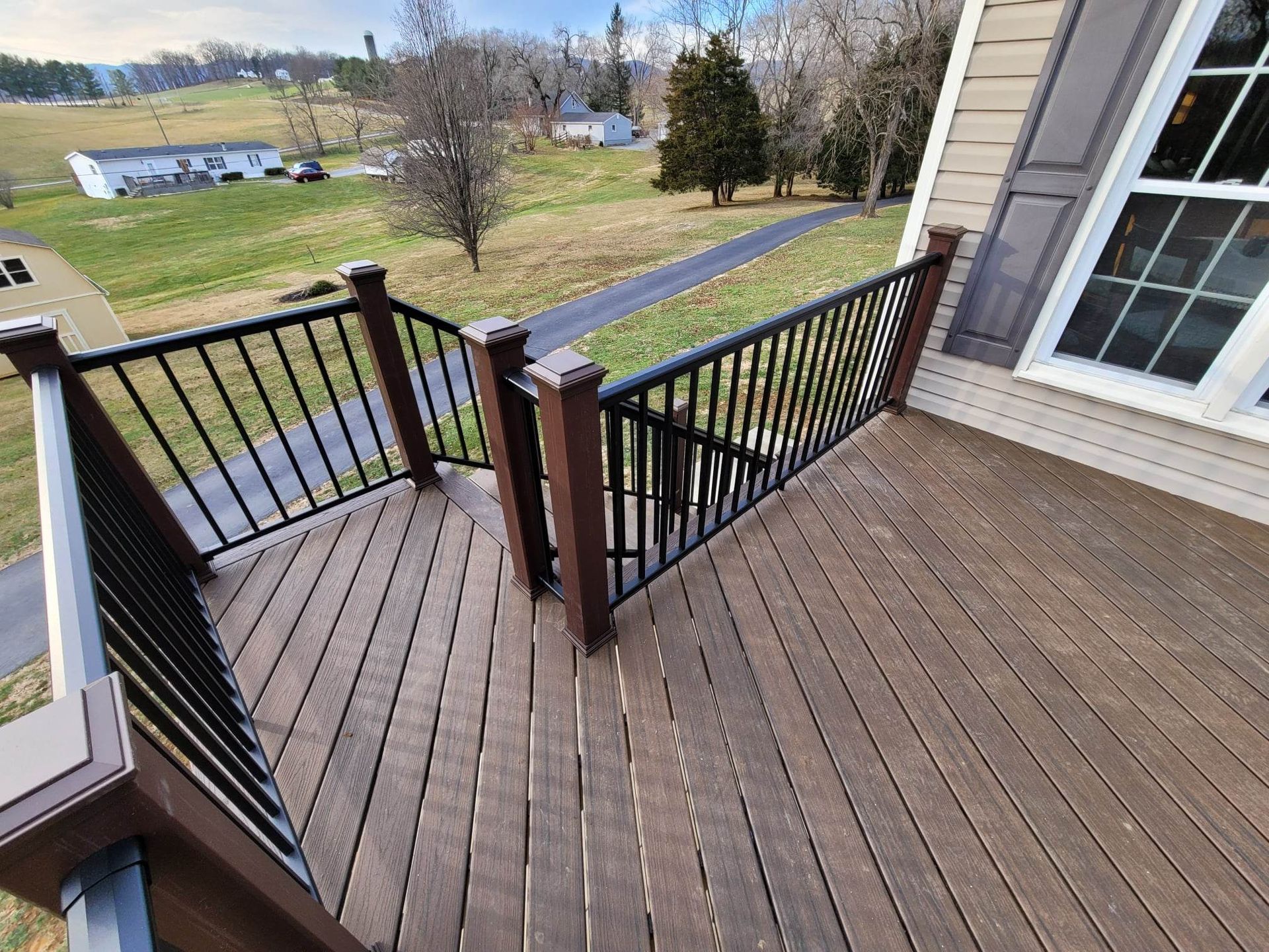 A wooden deck with a black railing and stairs leading up to it.