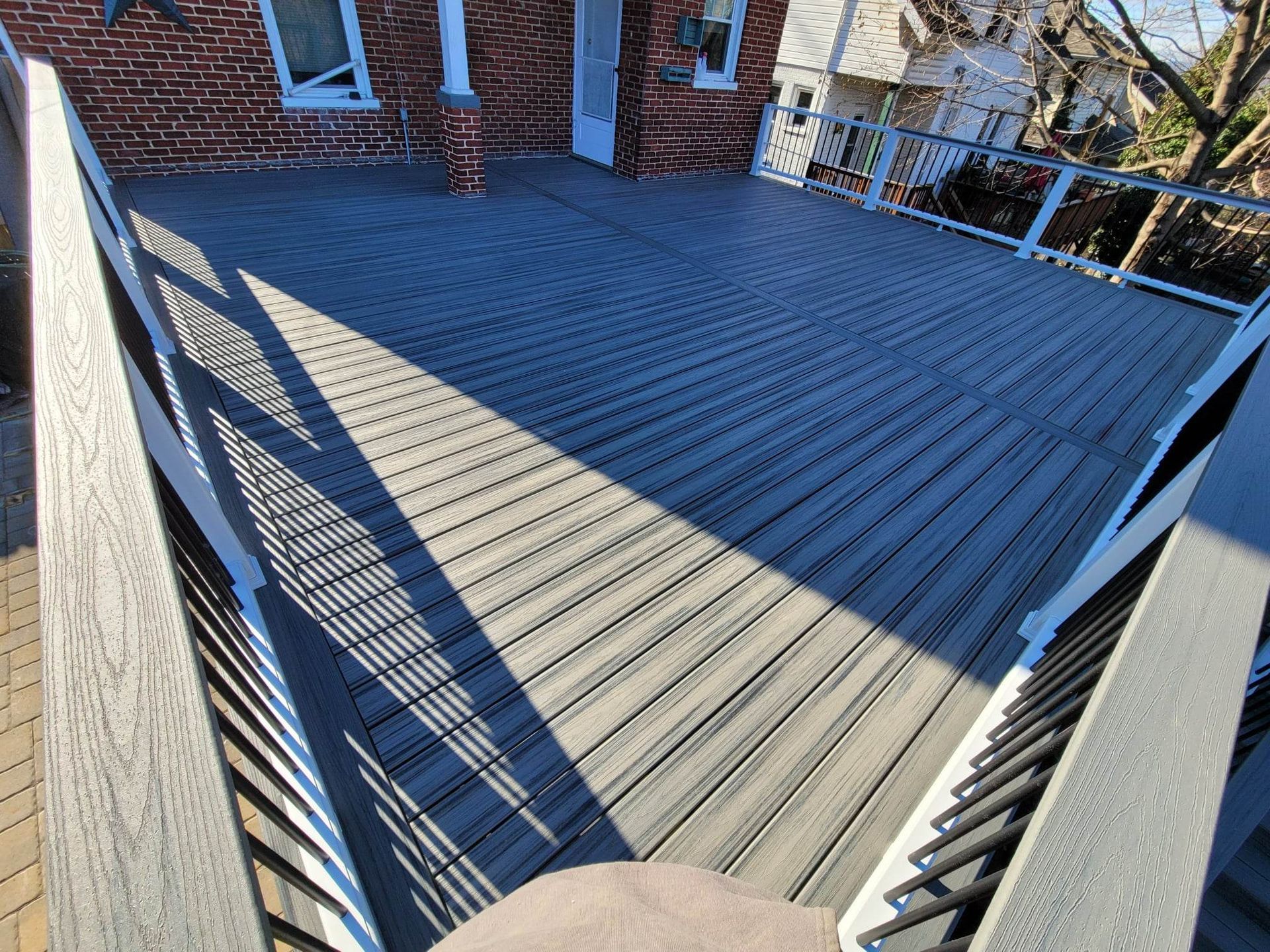 A gray deck with a white railing is in front of a brick building.
