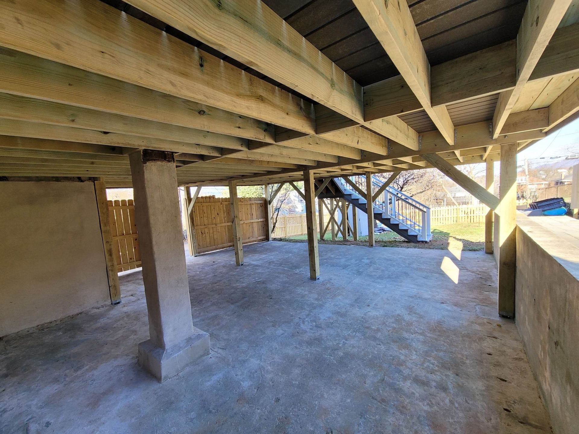 A concrete floor under a wooden deck with a staircase.