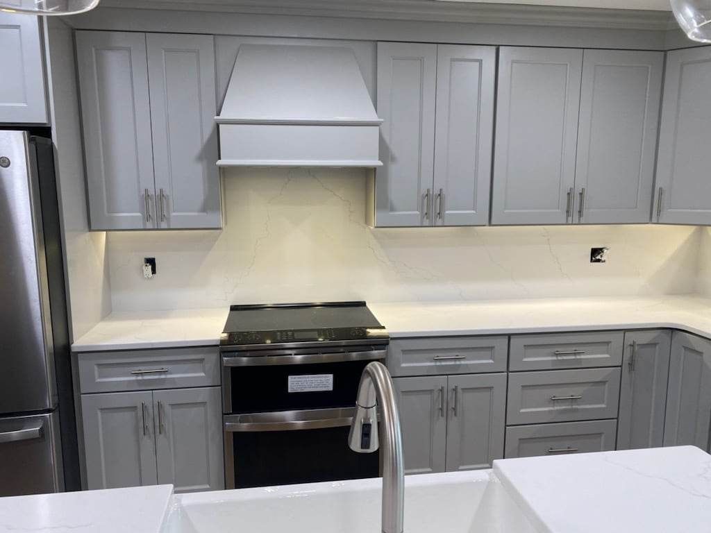 A kitchen with gray cabinets , a stove , a sink , and a refrigerator.