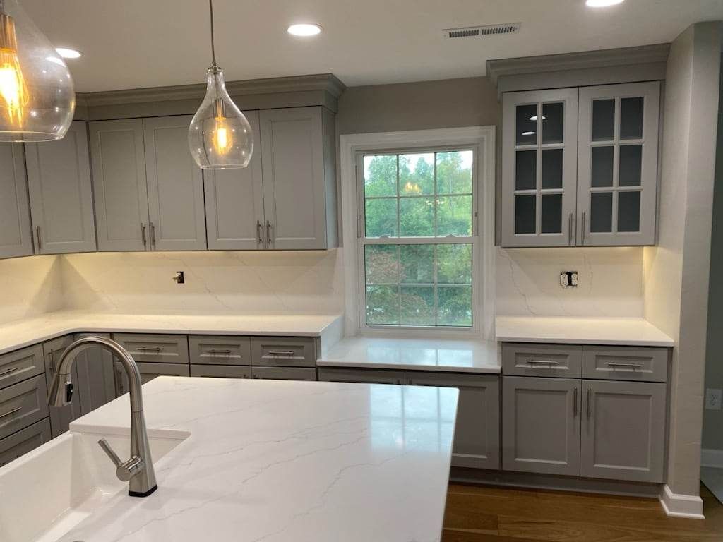 A kitchen with gray cabinets , white counter tops , a sink , and a window.