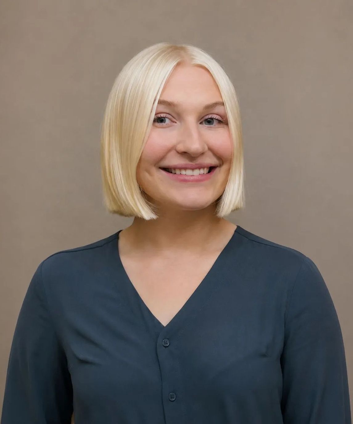 Person standing in a wooden staircase hall, wearing a light blazer and smiling at the camera.
