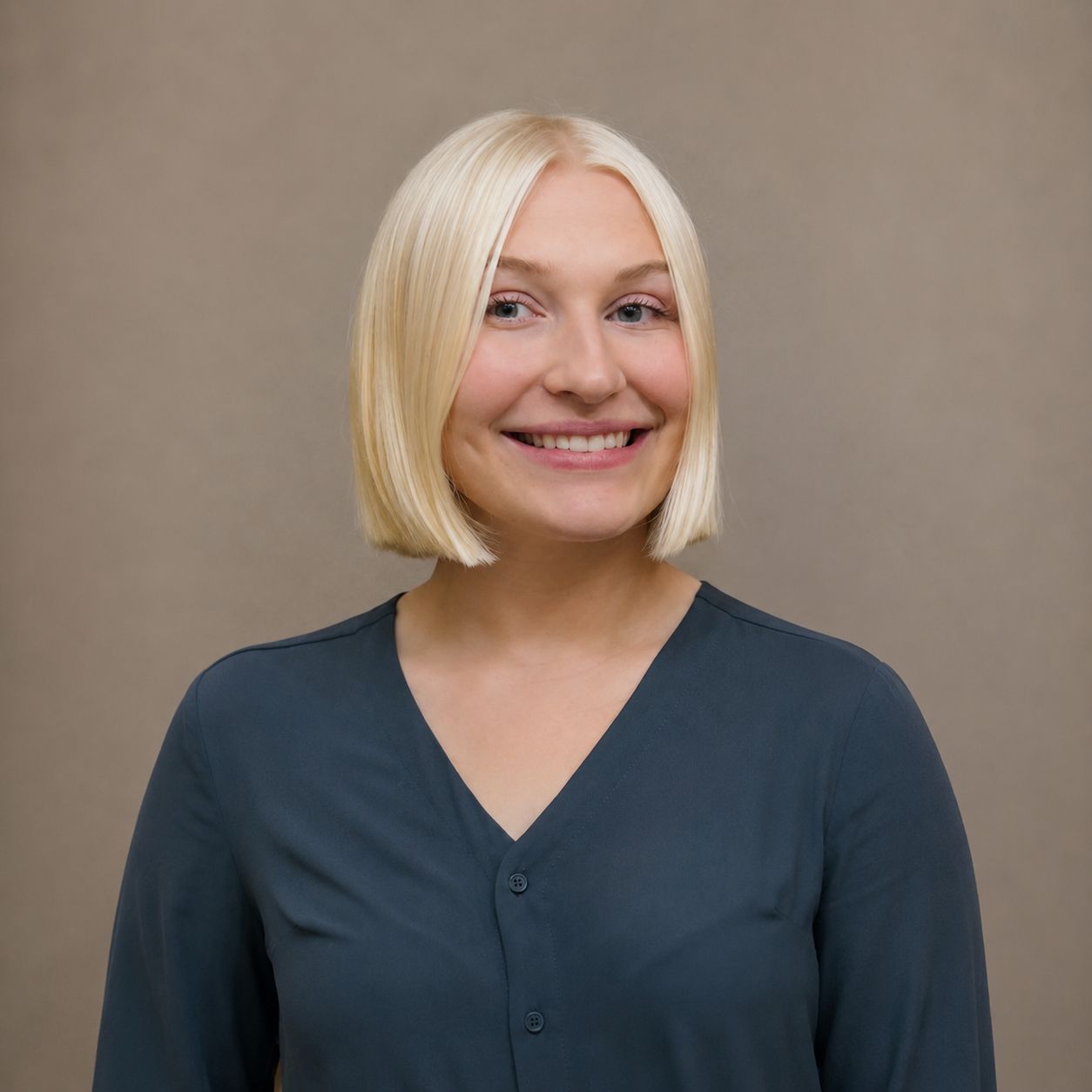 Person standing in a wooden staircase hall, wearing a light blazer and smiling at the camera.