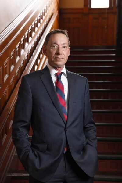 Man in dark suit and striped tie standing on a wooden staircase, hands in pockets
