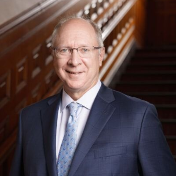 Man in a navy suit standing by a staircase, smiling at the camera