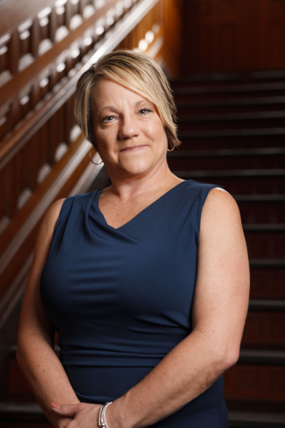 Woman in a blue sleeveless dress sitting on a staircase, looking at the camera.