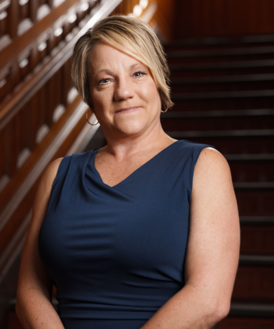 Woman in a blue sleeveless dress sitting on a staircase, looking at the camera.
