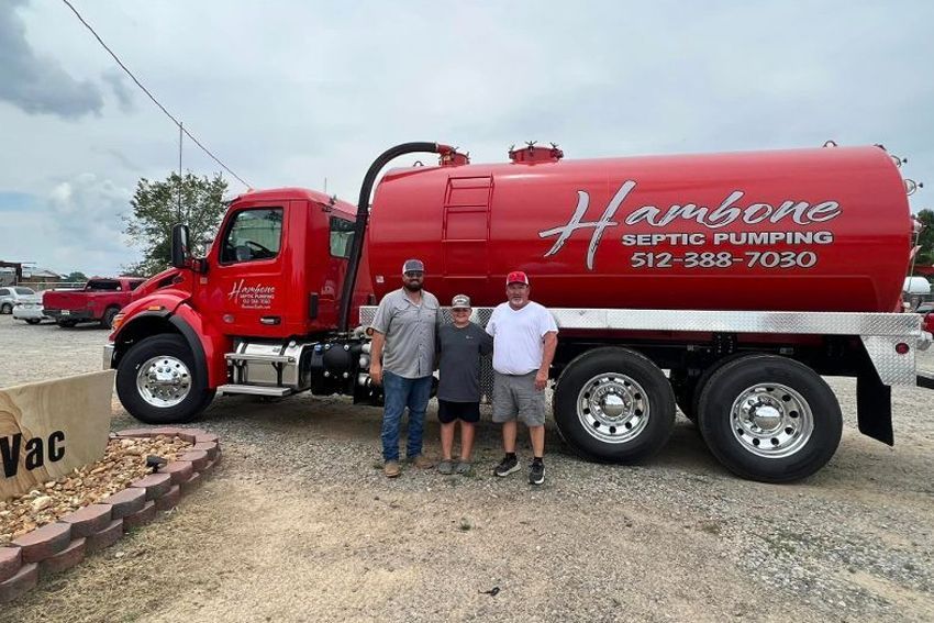 Three men are standing in front of a red septic pumping truck.