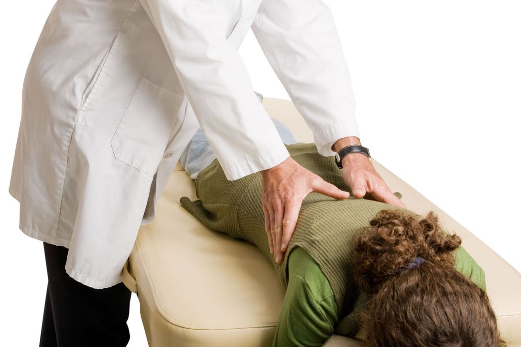 Doctor in white coat examining a patient's back on an examination table.