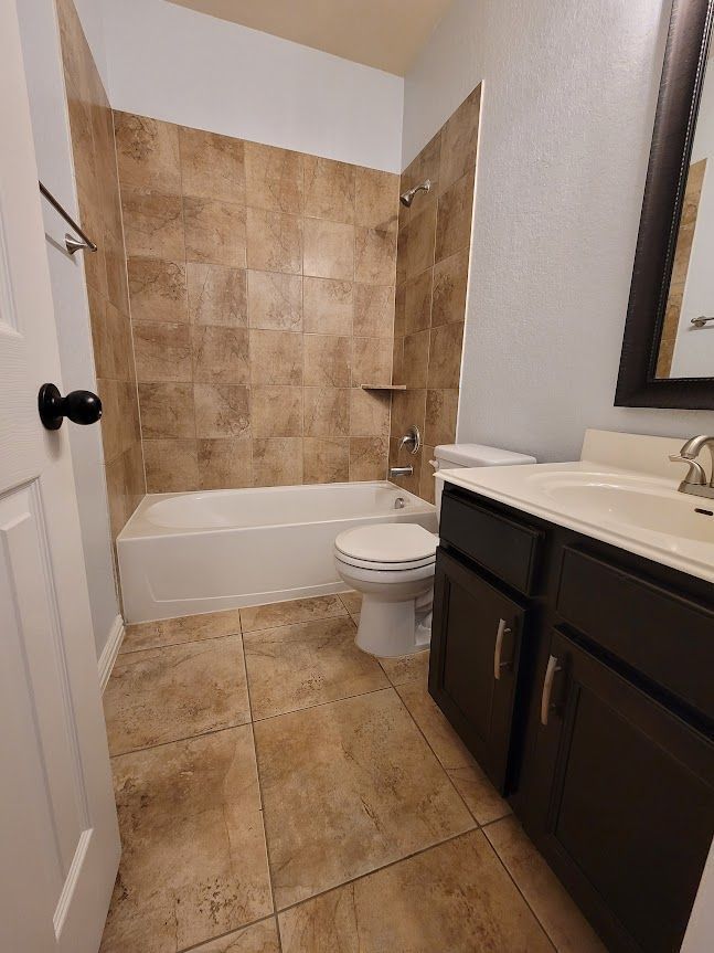 A bathroom with a tub, toilet, sink, and mirror.