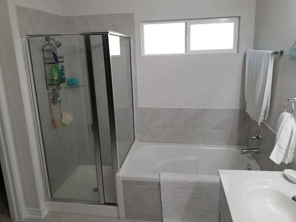 A bathroom with a tub, sink, shower, and window.