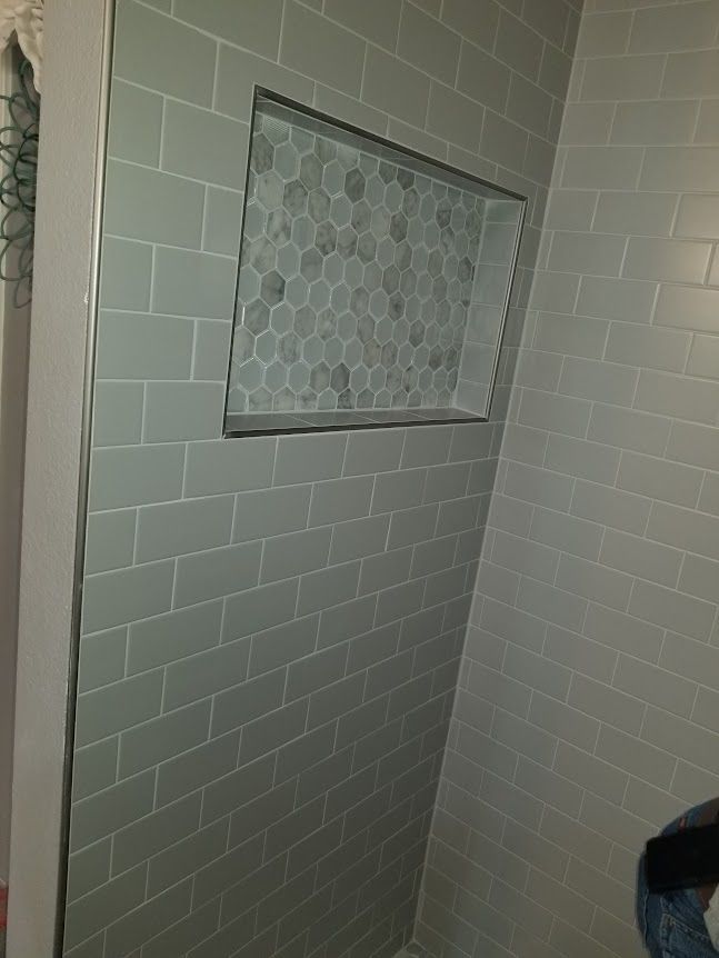 A person is standing in a bathroom with a brick wall and a niche in the shower.