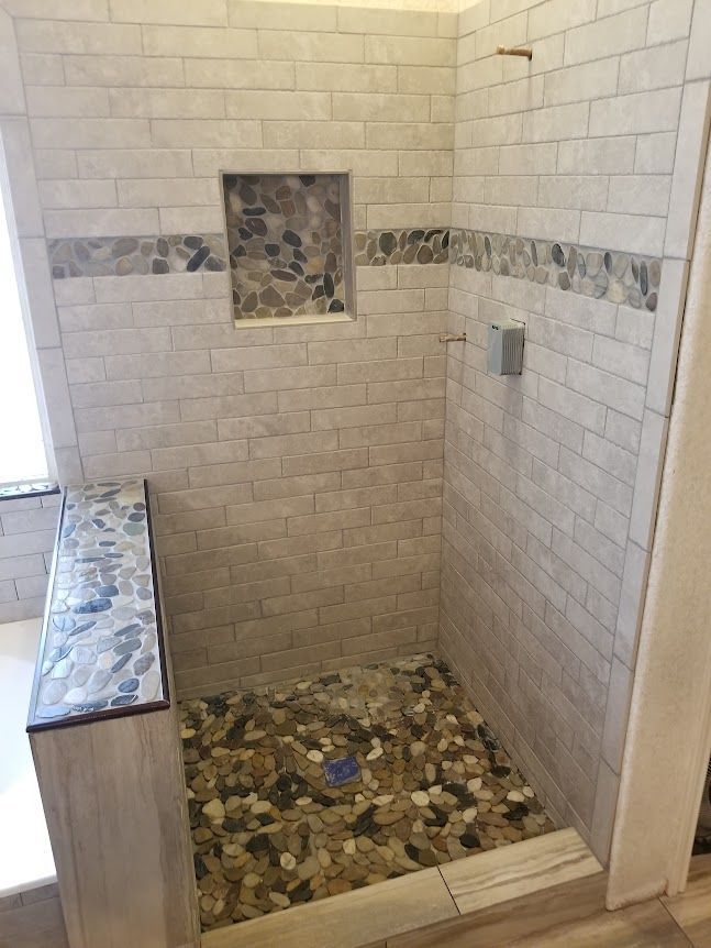 A walk in shower with a tiled floor and a window.