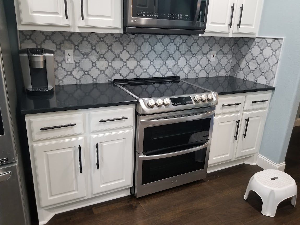 A kitchen with white cabinets, a stove, a microwave, and a stool.