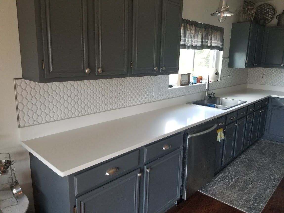 A kitchen with gray cabinets and white counter tops.