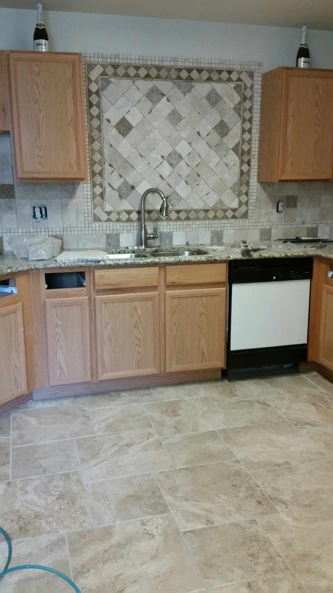 A kitchen with wooden cabinets , granite counter tops , a sink and a dishwasher.