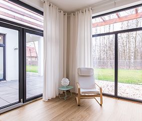 There is a chair in the corner of the room with a lot of windows.
