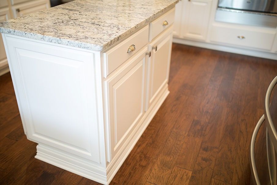 A kitchen island with a granite counter top and white cabinets.