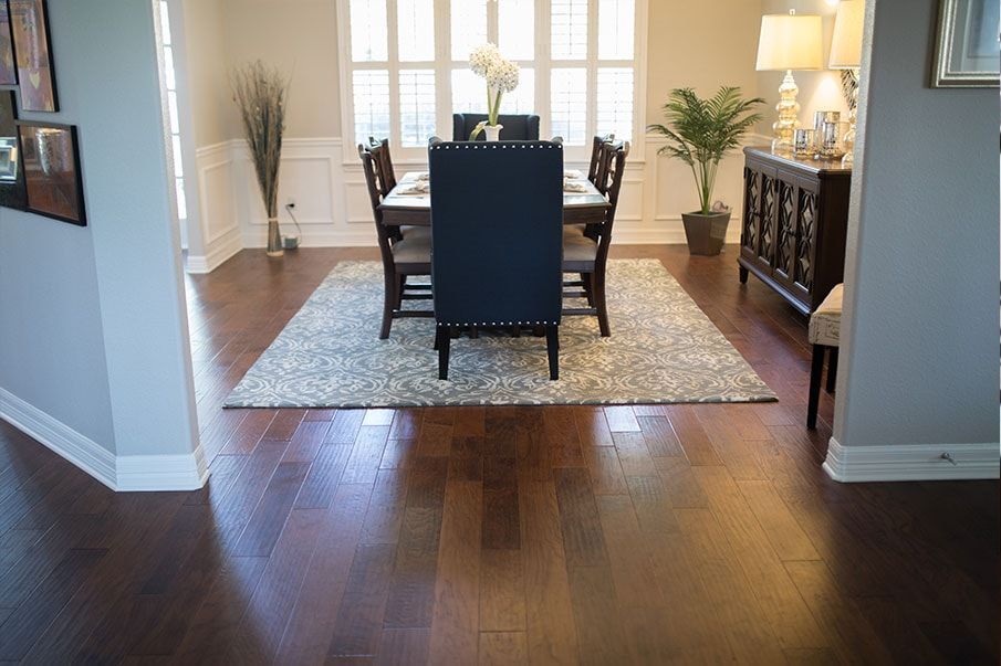 A dining room with a table and chairs and a rug on the floor.