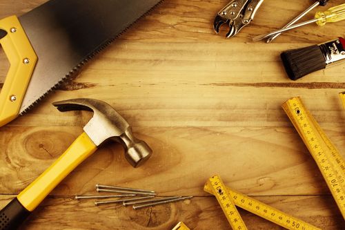 Hammer, ruler, nails, and measuring tools on a wooden workbench with a saw and brush nearby