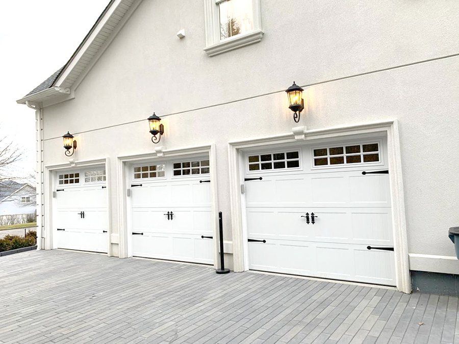 Three white garage doors are lined up on the side of a house.