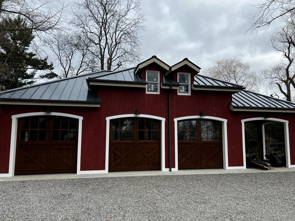 A red barn with three garage doors and a metal roof.