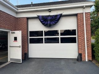 A brick building with a white garage door and a purple flag hanging from the roof.
