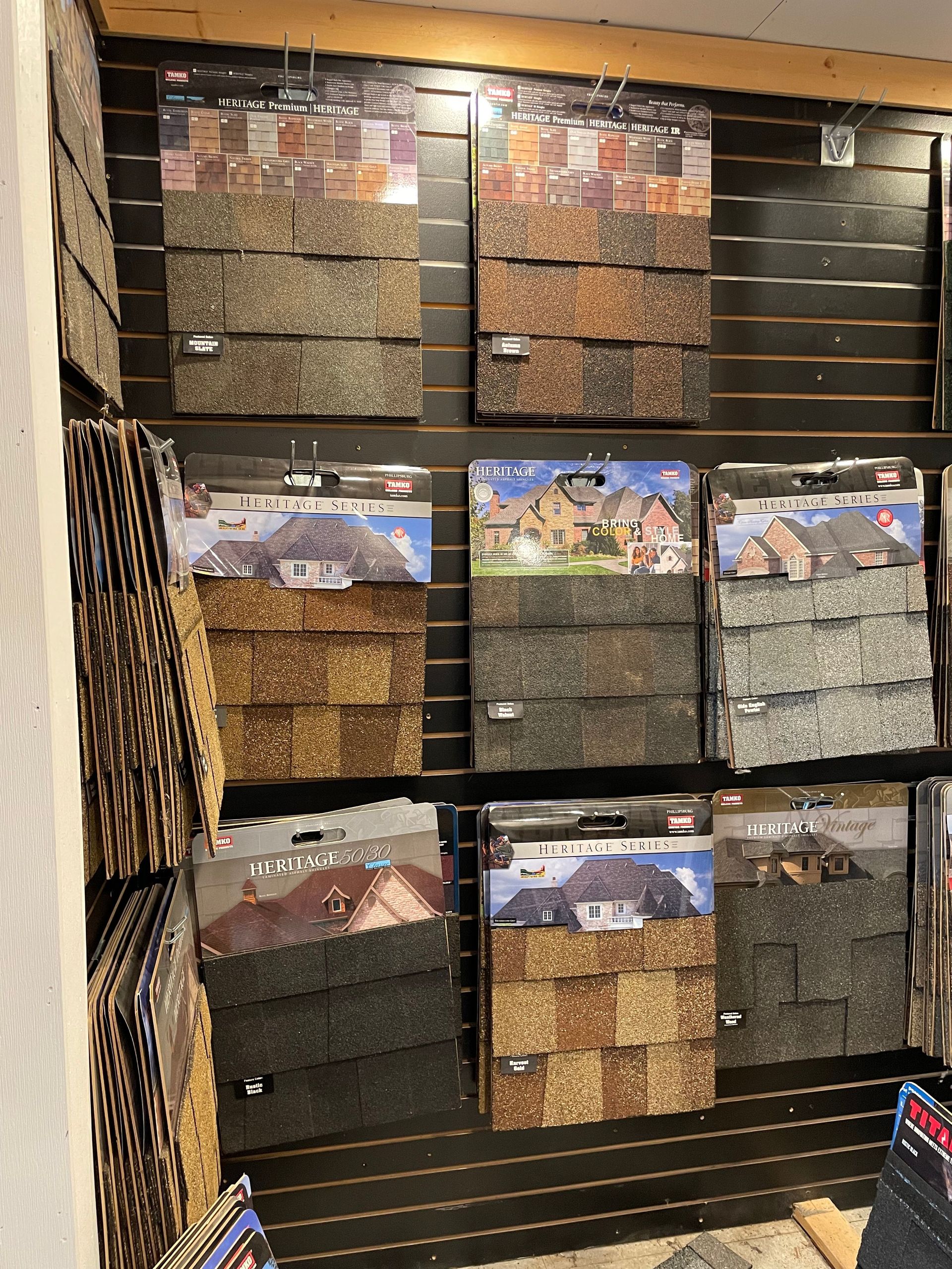 Displays of various roofing shingle samples in different colors on a wall.