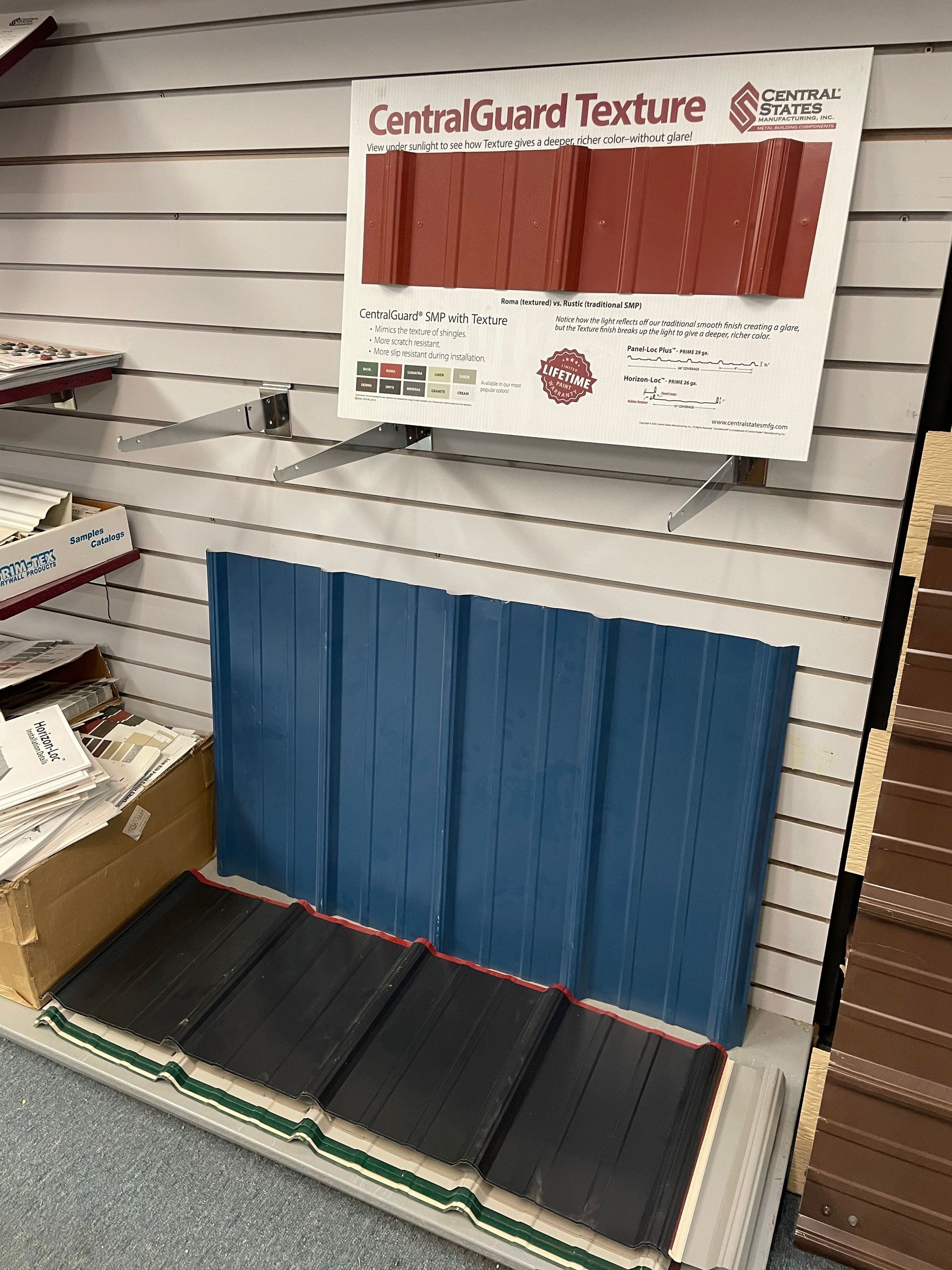Display of metal roofing samples in various colors on a store wall. Includes blue, red, and dark panels.