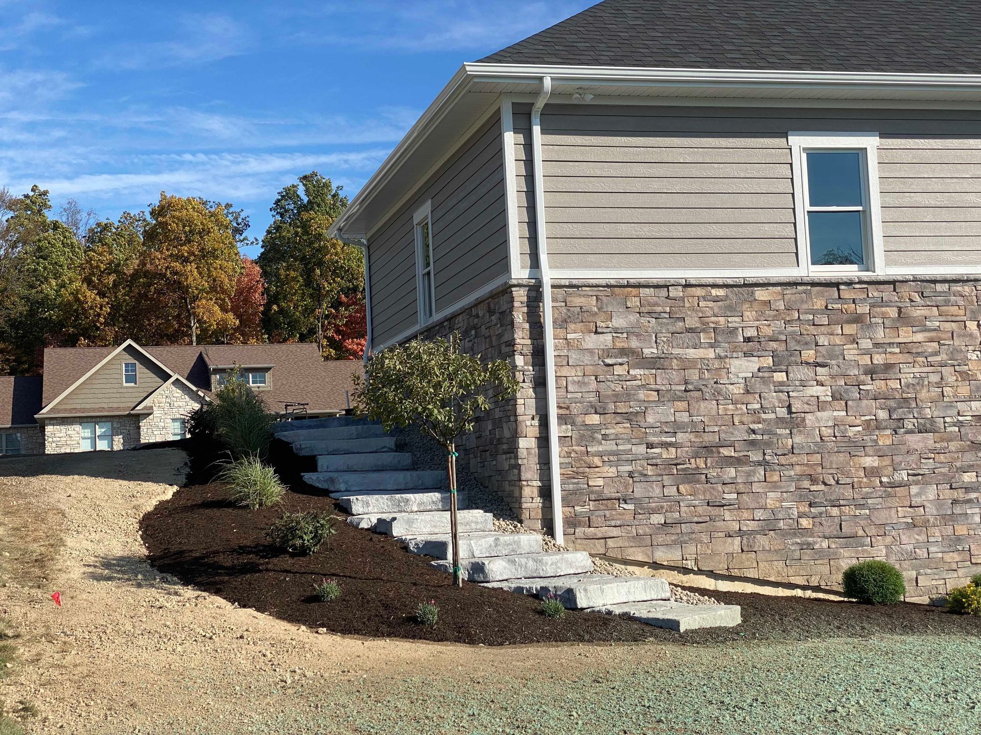 Stone steps lead up to a house with stone and siding. Mulch and landscaping surround the steps.