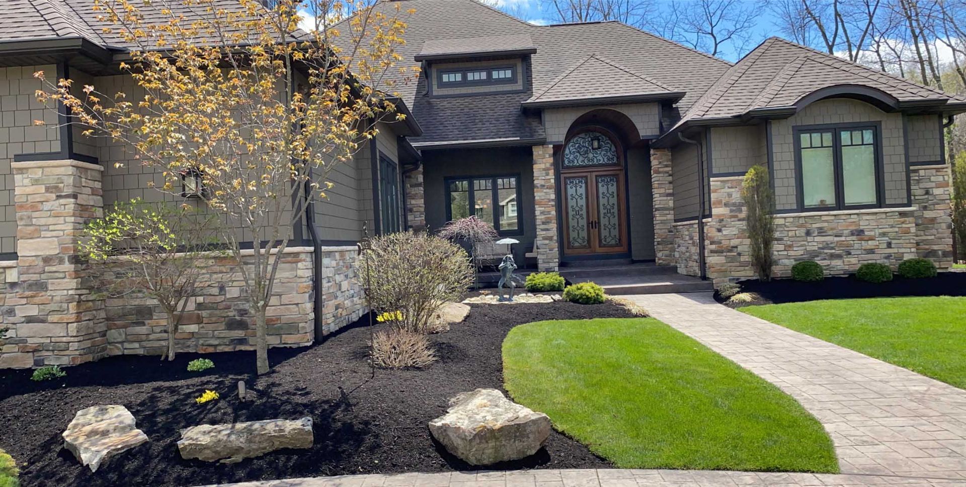 A stone-accented home with a walkway, surrounded by green grass and dark mulch.