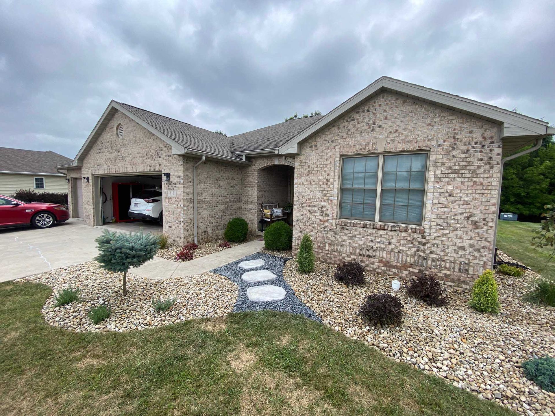 Brick house with attached garage, landscaped yard, stone walkway leading to the front door, cloudy sky.