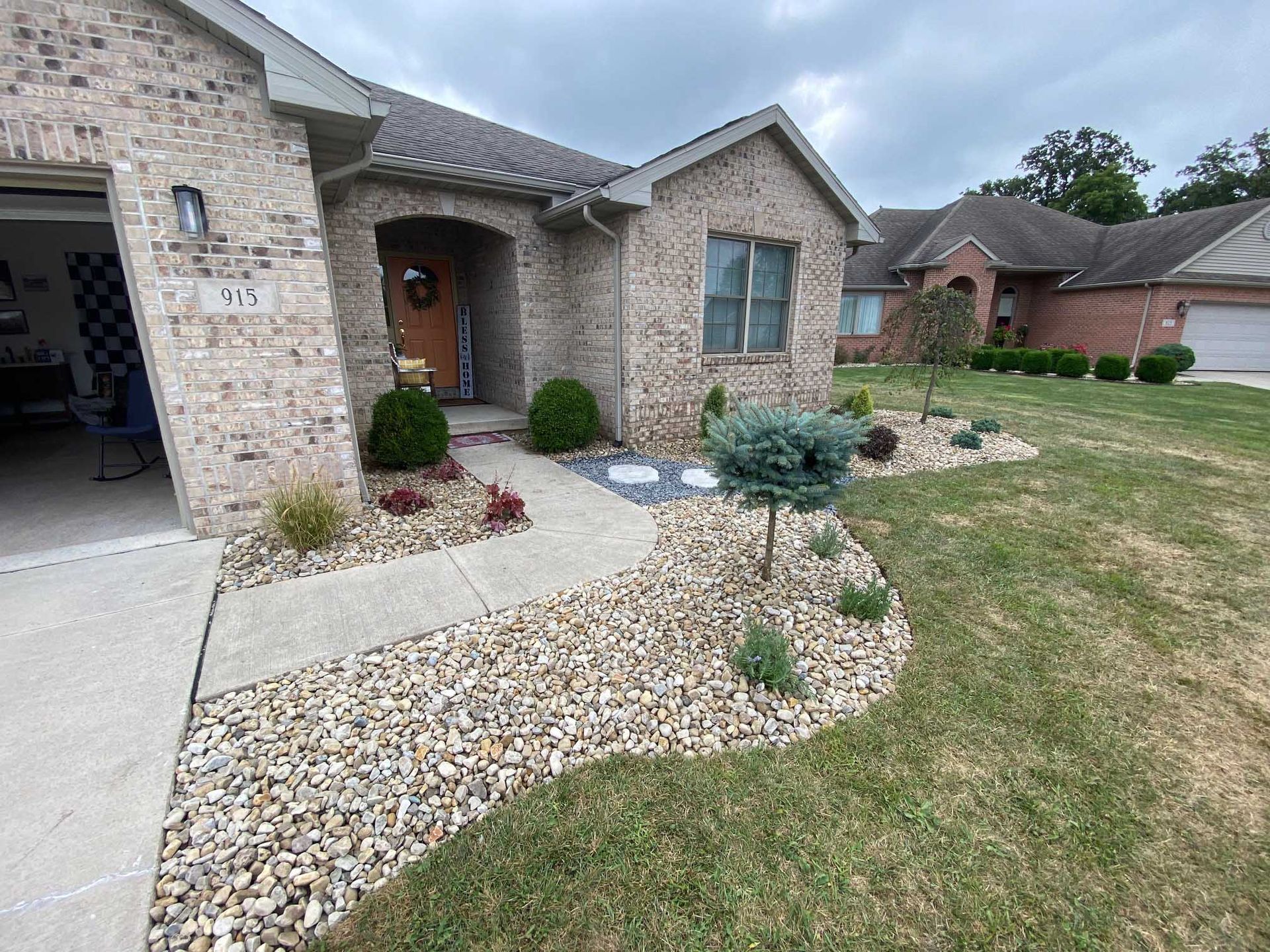 Beige brick house with walkway and landscaped yard, front door with wreath, and gravel borders.