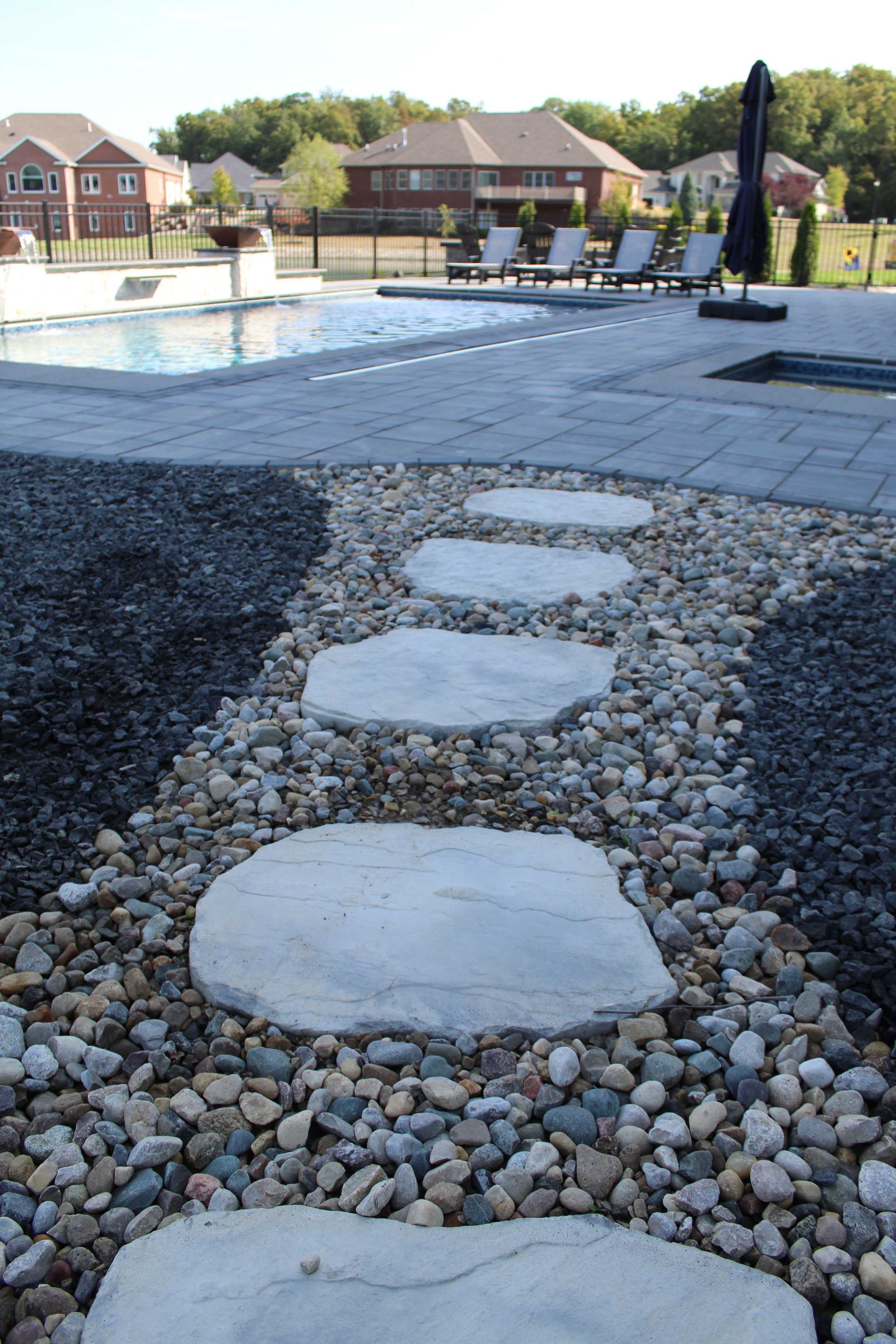 Stone pathway with stepping stones, surrounded by gravel, leading to a pool in a residential backyard.