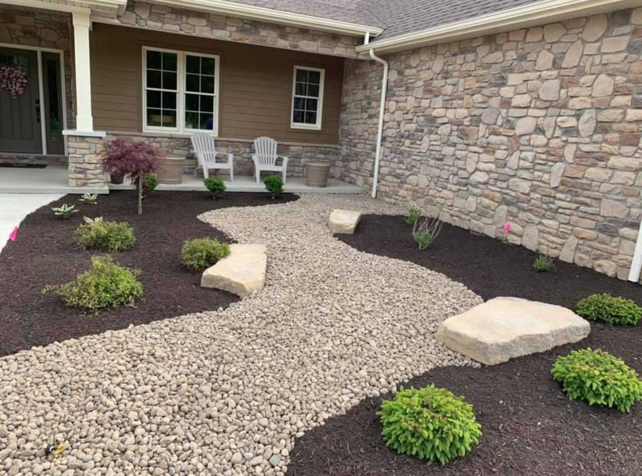 Stone path winds through landscaped front yard with green bushes and stone wall.