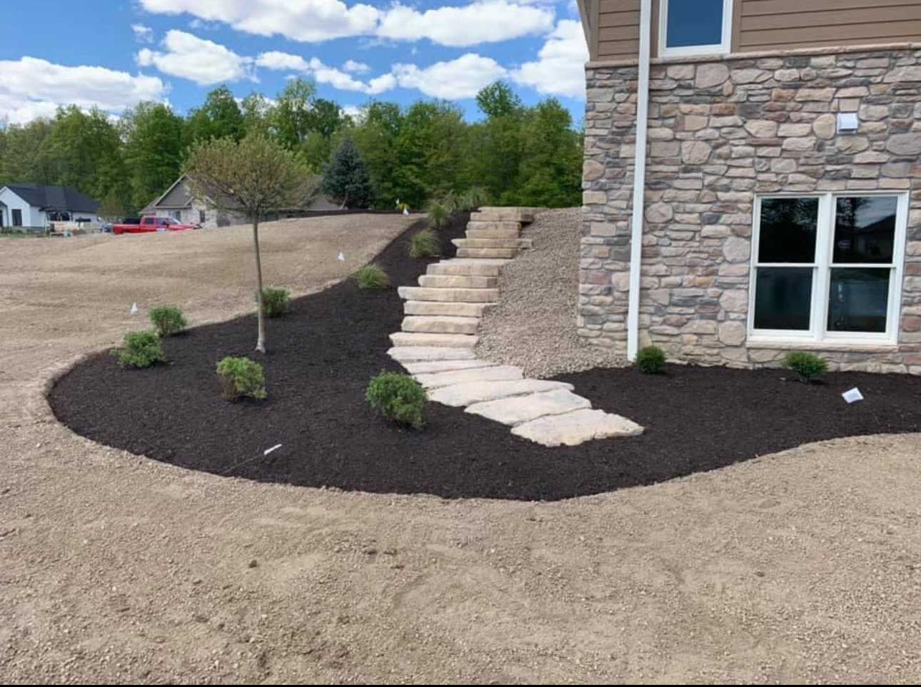 Newly landscaped front yard with stone steps, mulch beds, and a stone-covered house.
