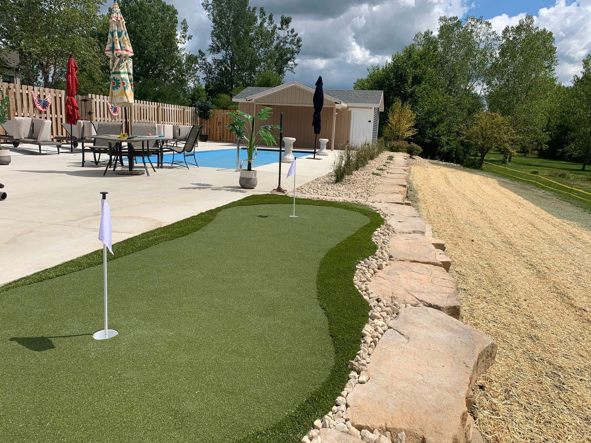 Miniature golf green next to a pool area with flags and artificial turf, sunny outdoor setting.