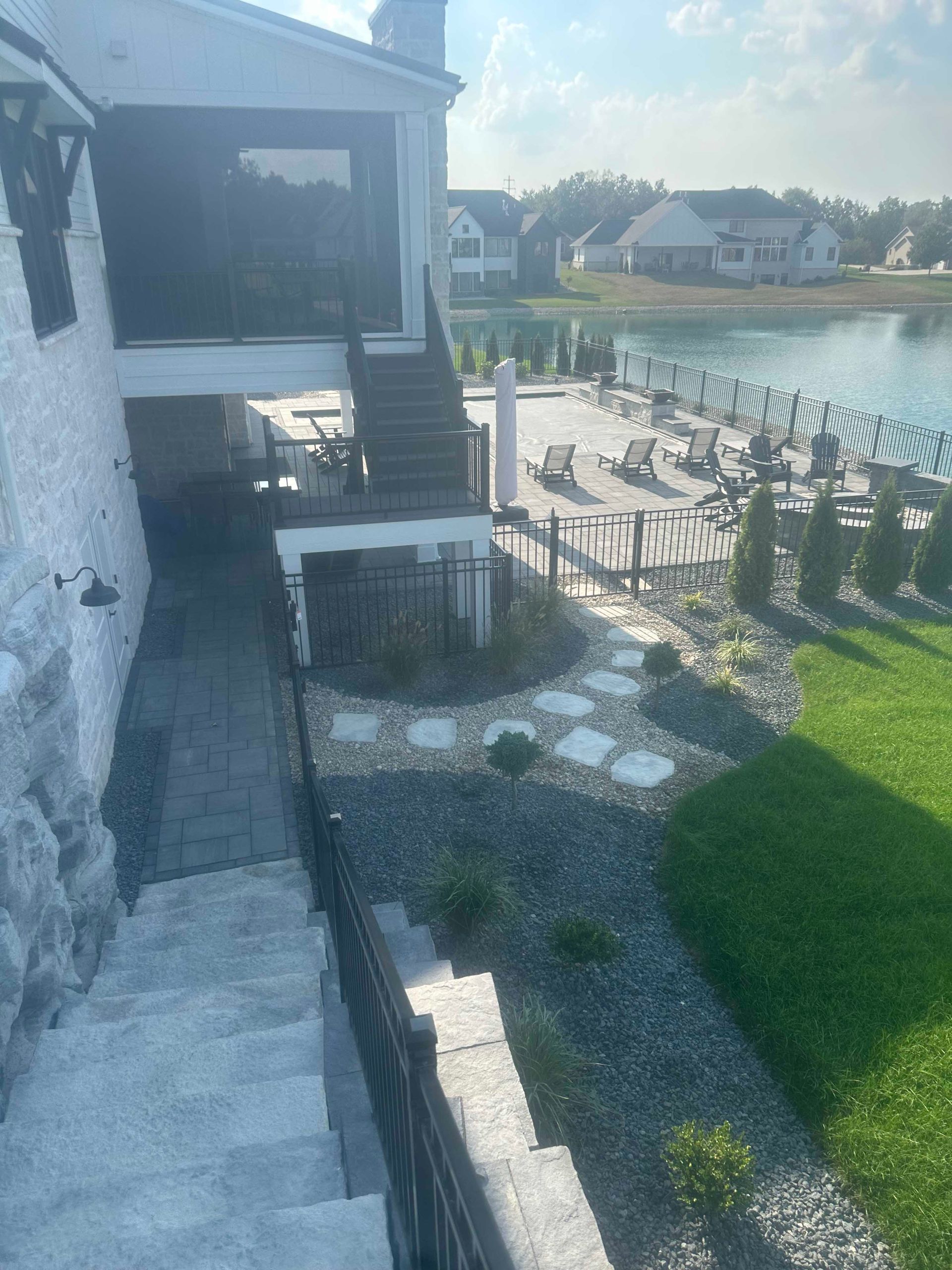 Exterior of a lakeside house with a deck and stone pathway. Grass and water visible.