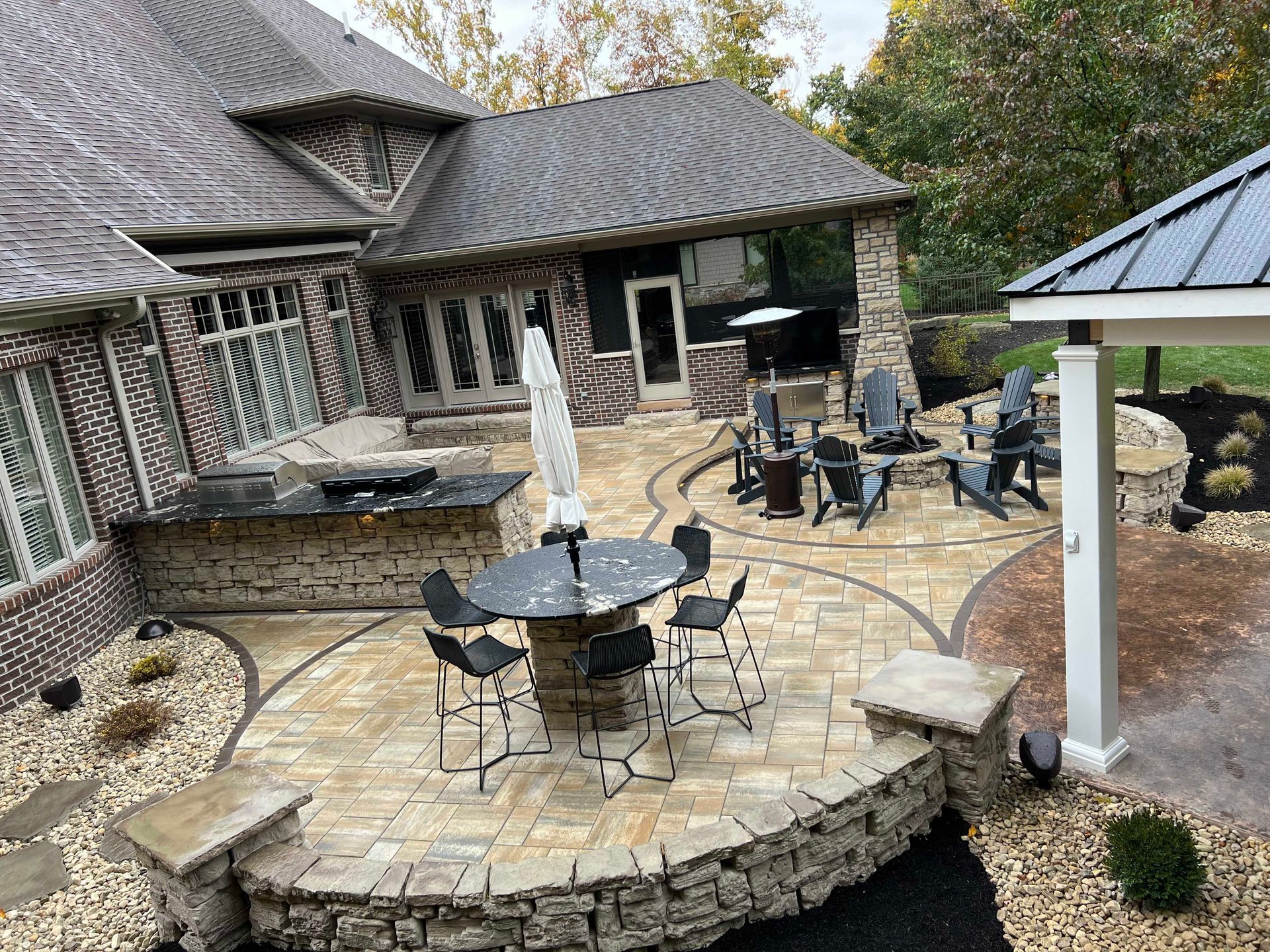 Patio with stone pavers, seating areas, outdoor kitchen, and fire pit.