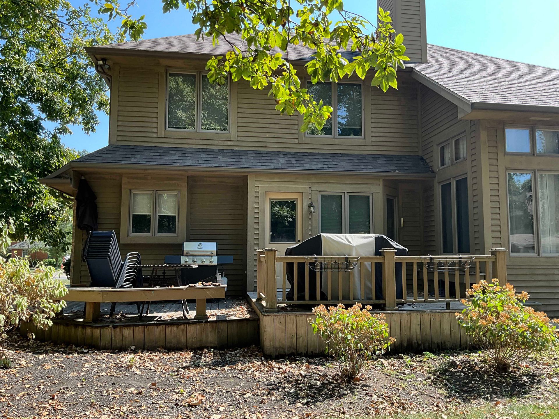 Rear view of a two-story home with wooden siding and a deck with a grill and outdoor furniture.