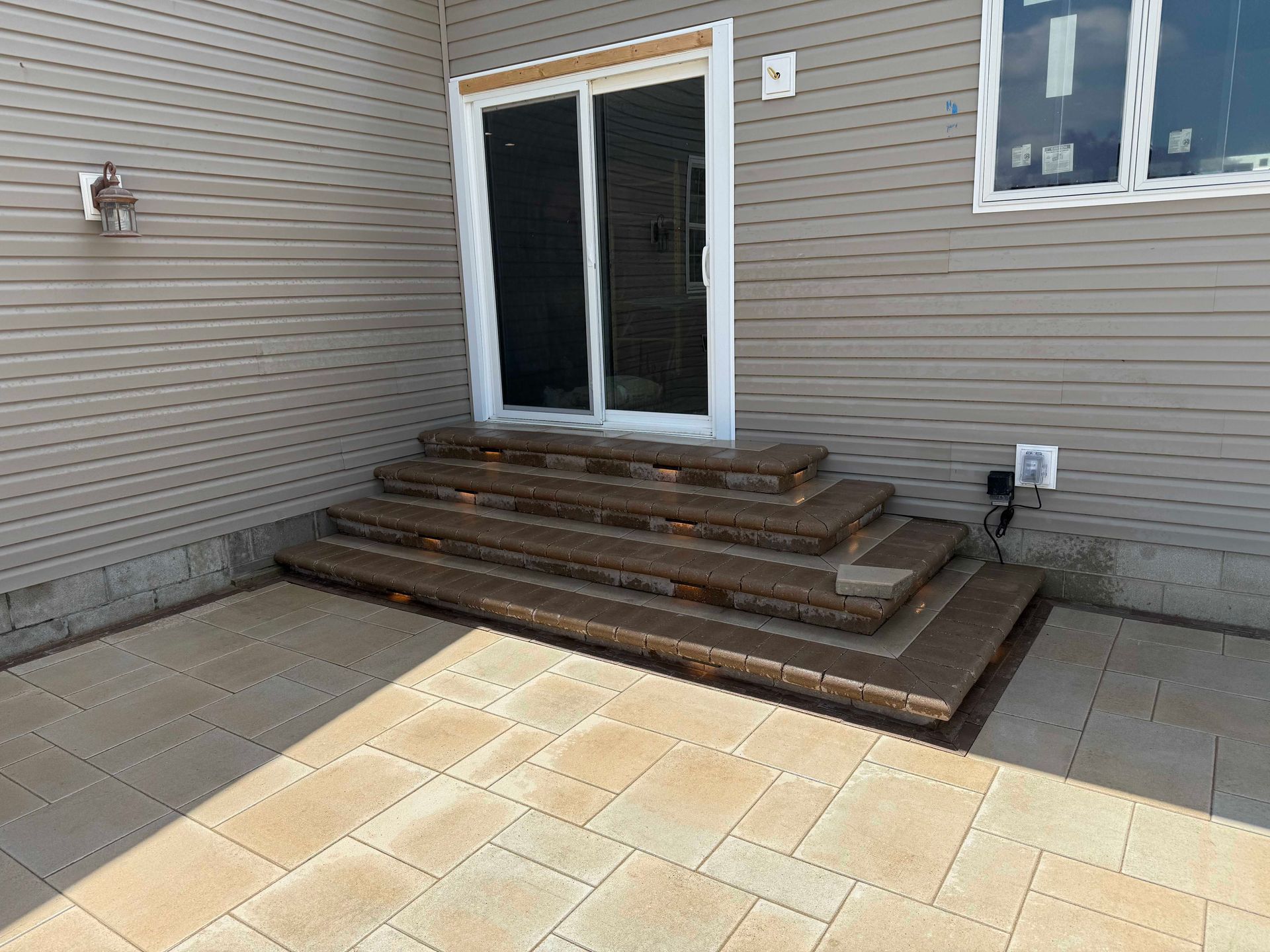 Stone steps leading up to a sliding glass door on a house with beige siding and a stone patio.