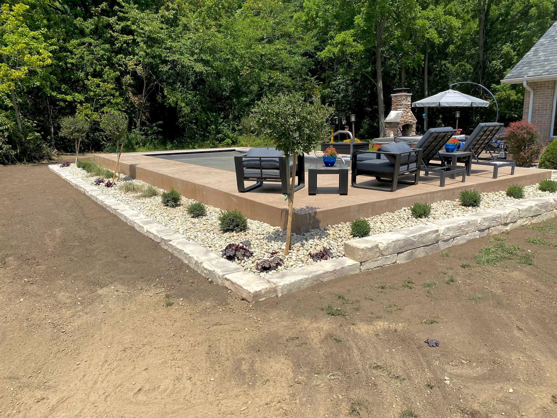 Pool patio with seating, landscaping with bushes and rock border, in backyard setting.