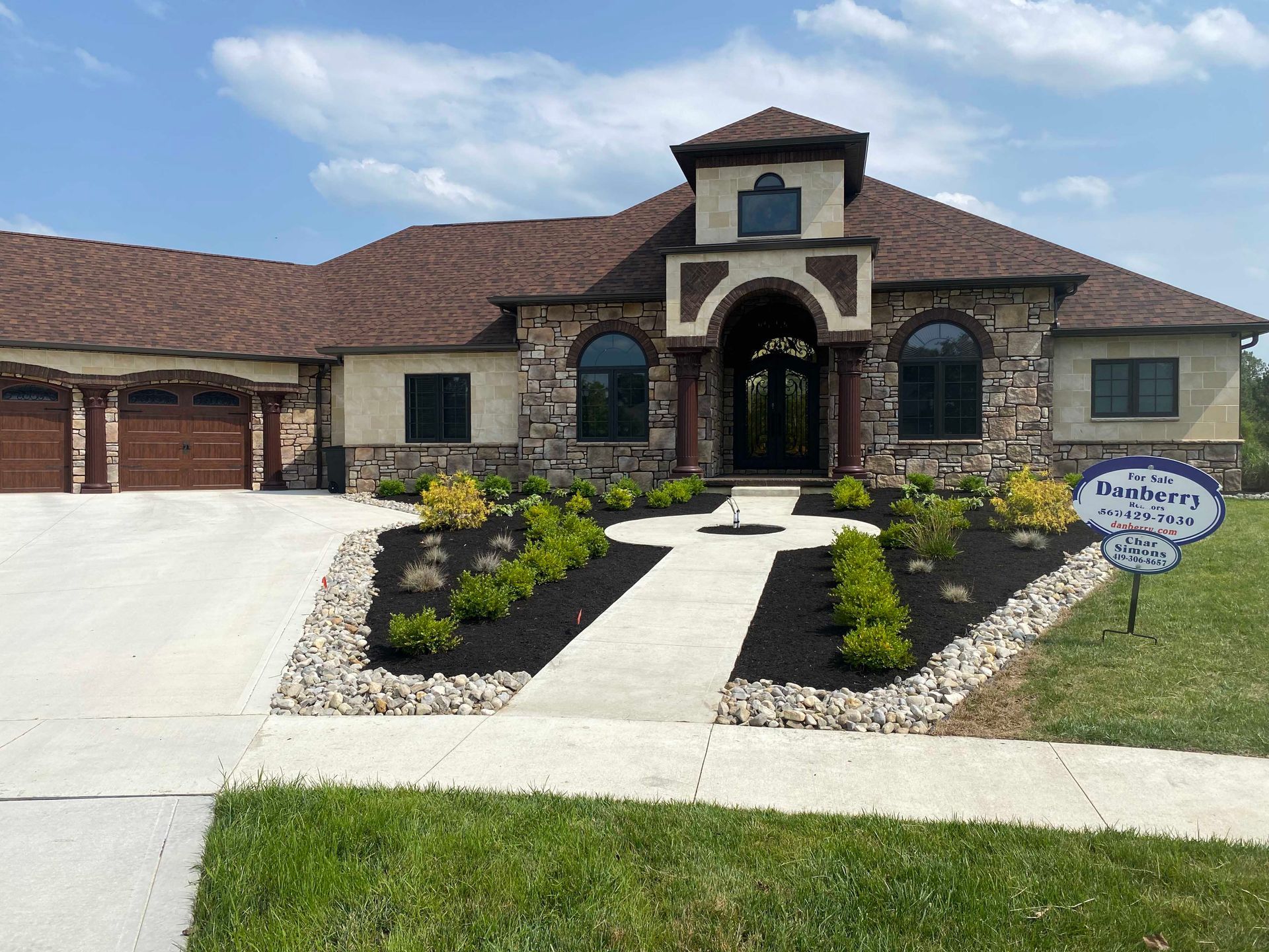Luxury home with stone and stucco exterior, landscaped front yard, and driveway.