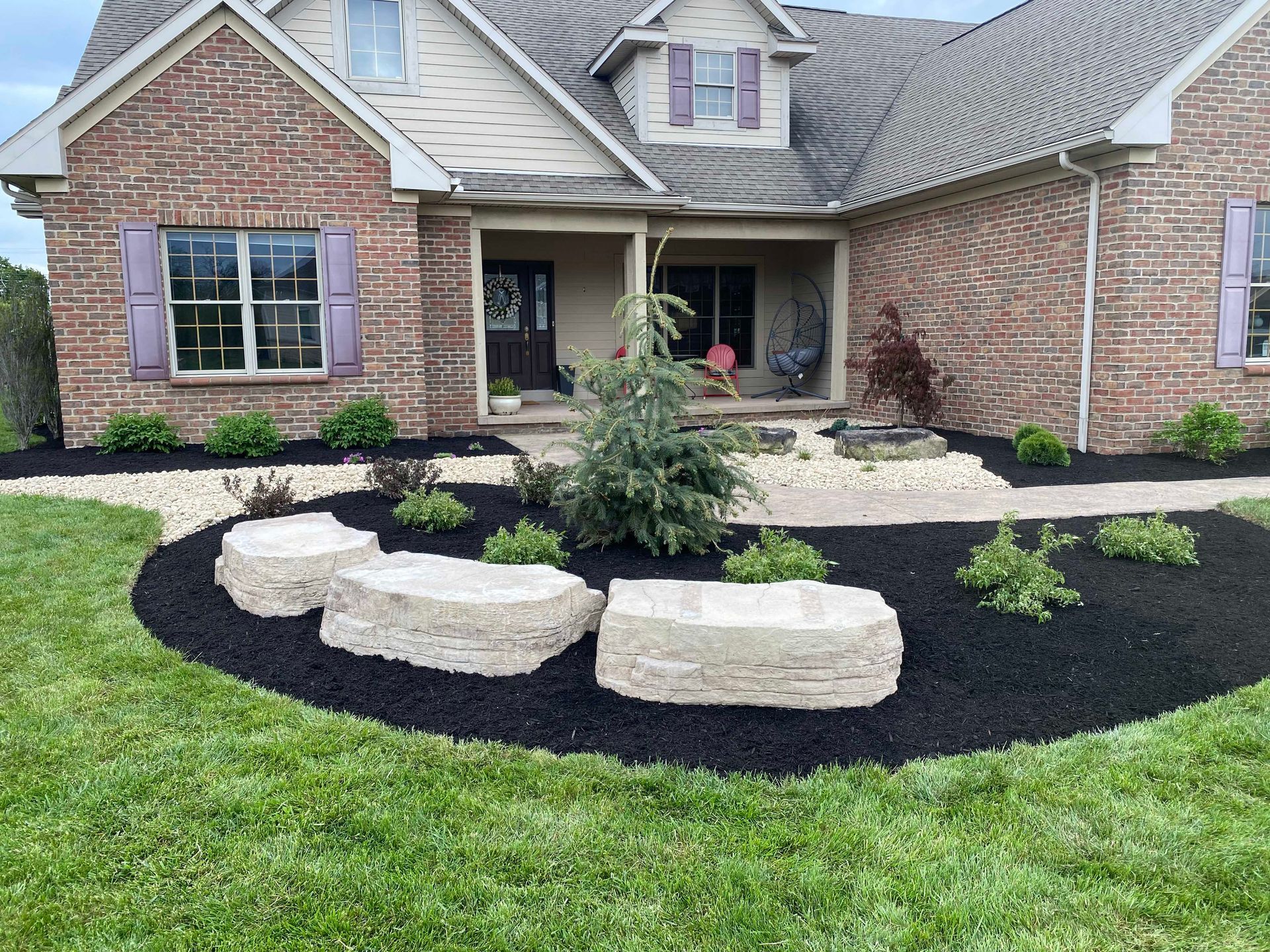 Landscaped front yard with dark mulch, stone accents, and a brick house.