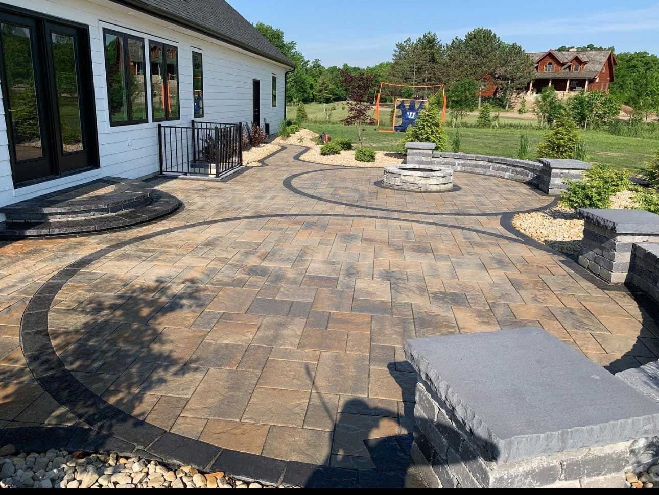 Brick patio with circular design, fire pit, and seating next to a white house.