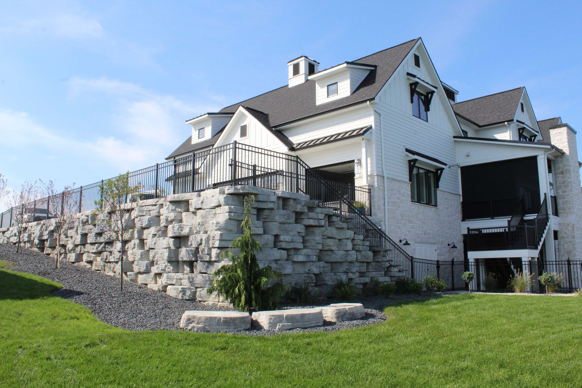White house with black roof and stone retaining wall.