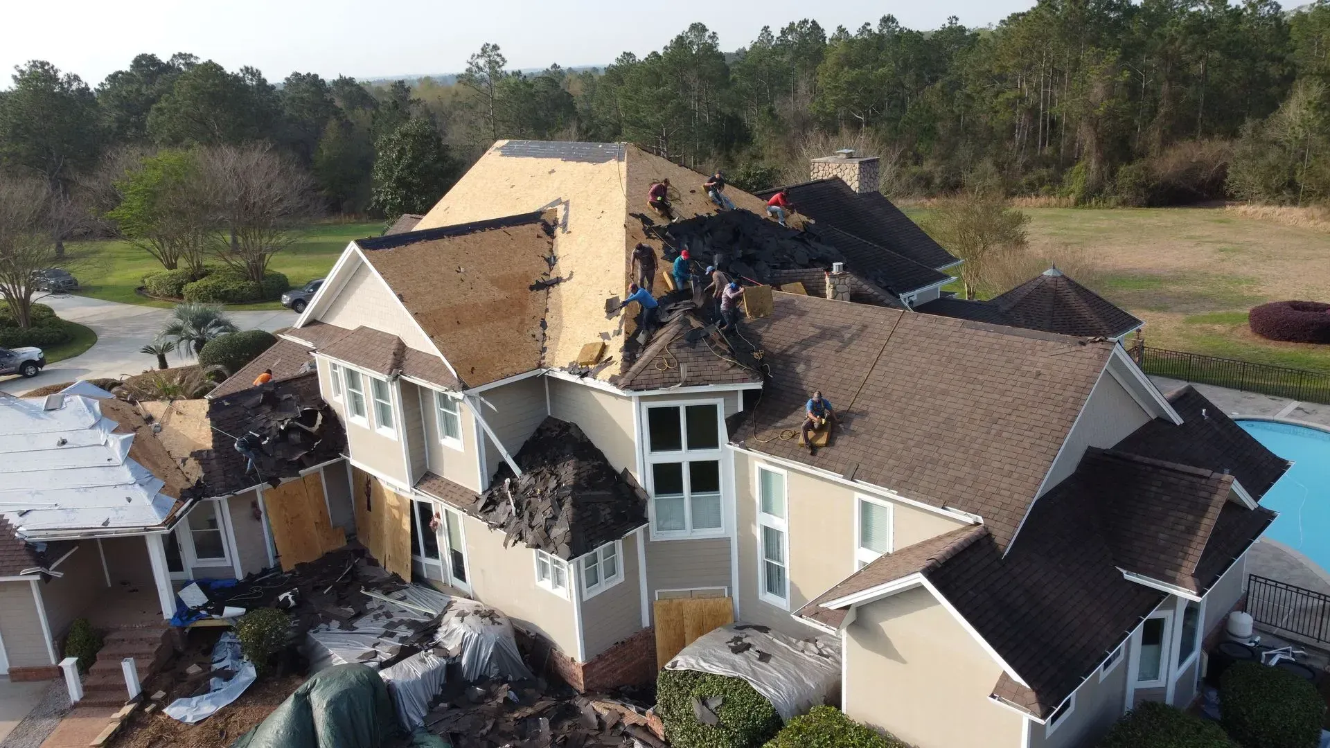 Roofers working on a house roof, removing old shingles and installing new ones, next to a pool.