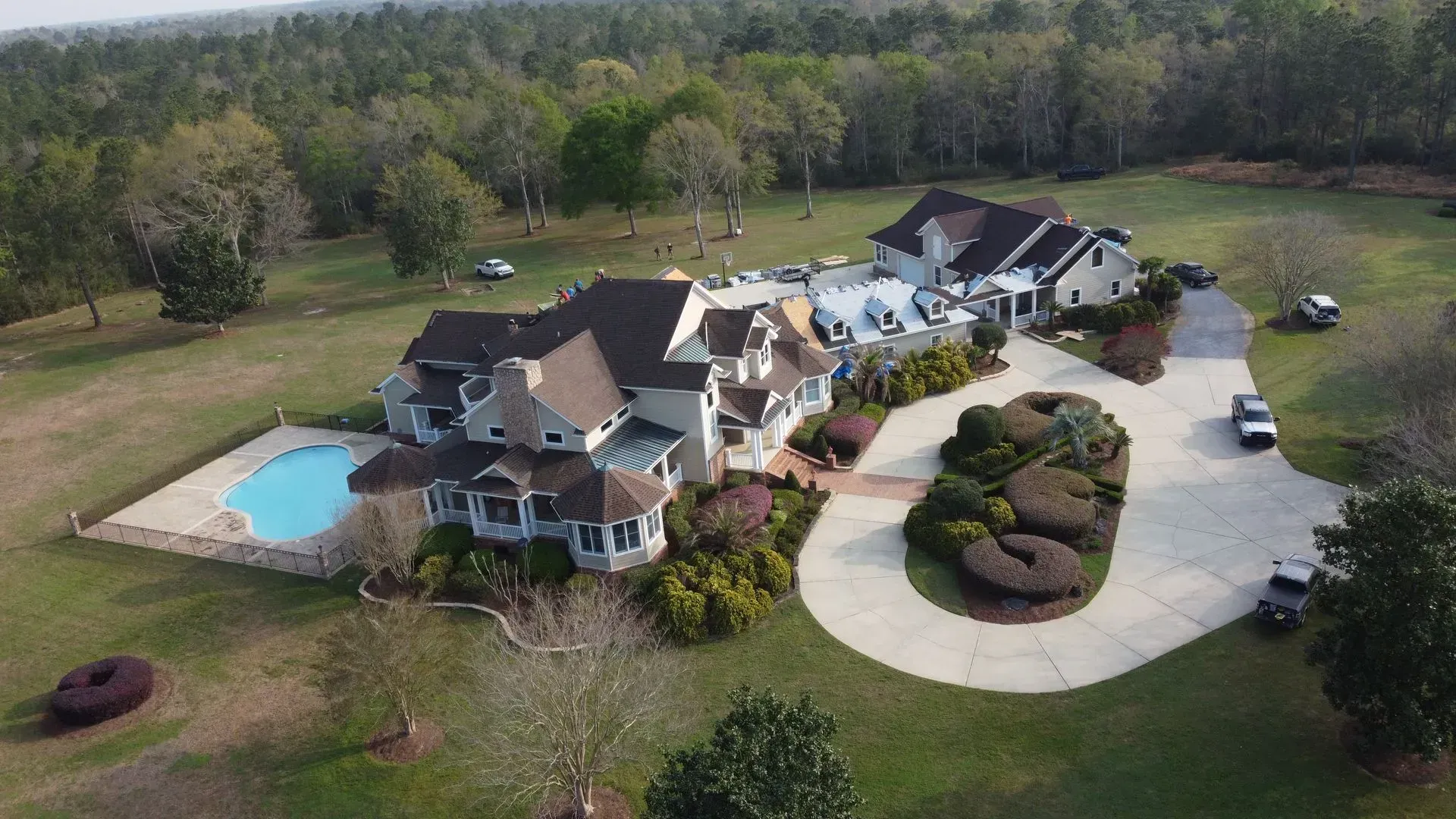 Aerial view of a large house with a pool, surrounded by trees and a circular driveway.
