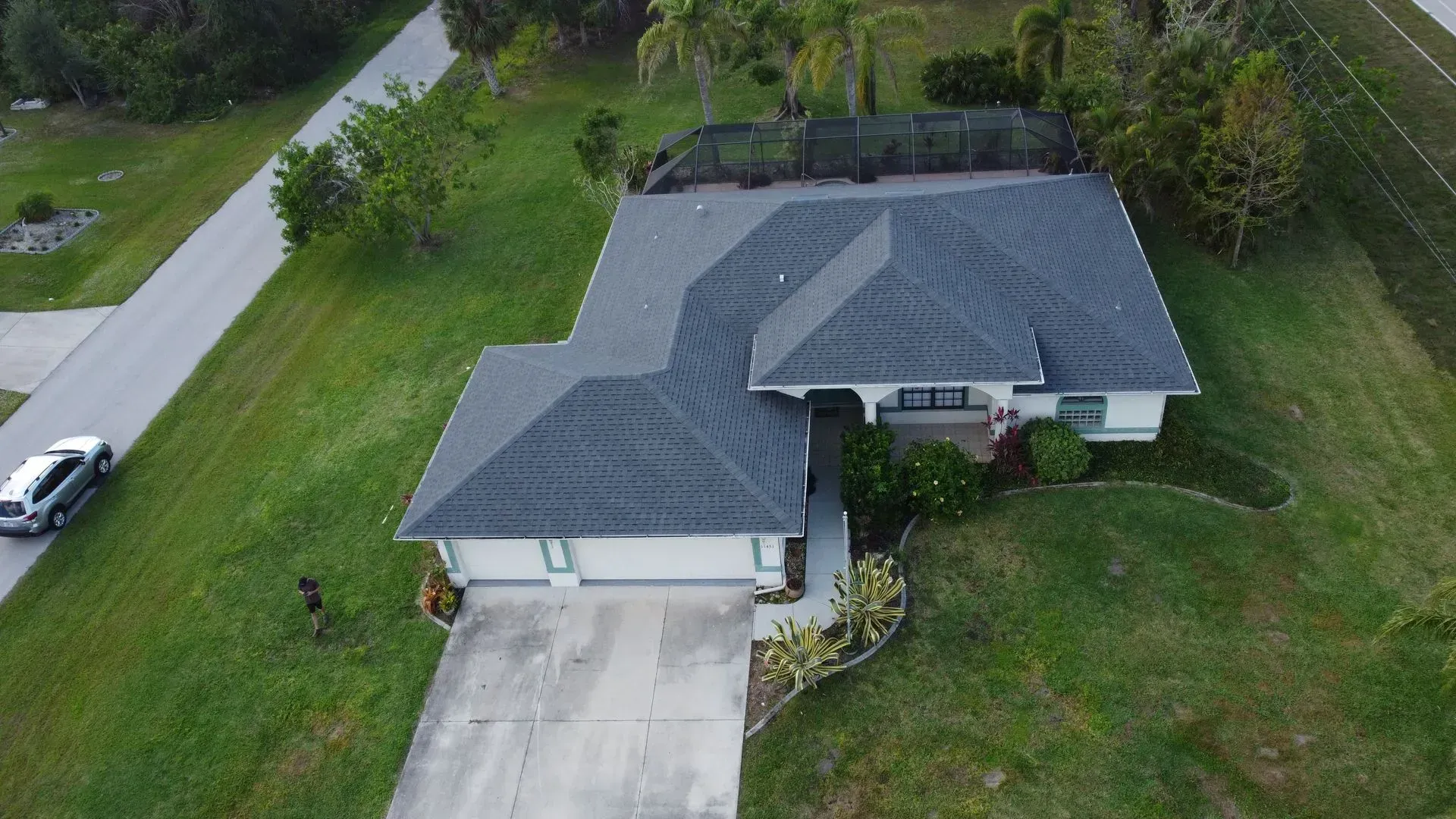 Aerial view of a white house with a gray roof and a driveway, surrounded by green grass and a road.