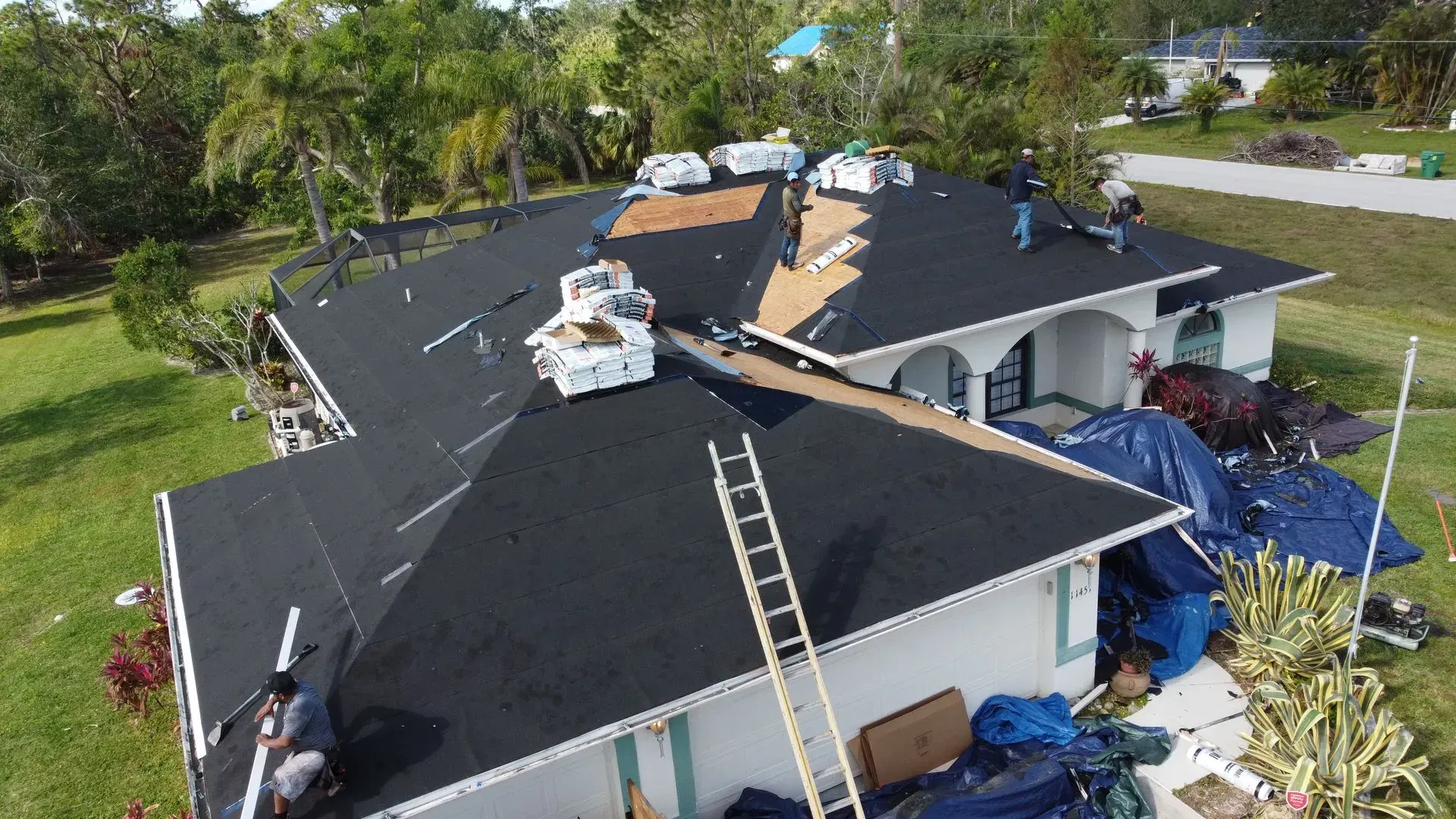 Roofers replacing shingles on a house; black asphalt shingles, ladders, and a utility vehicle.